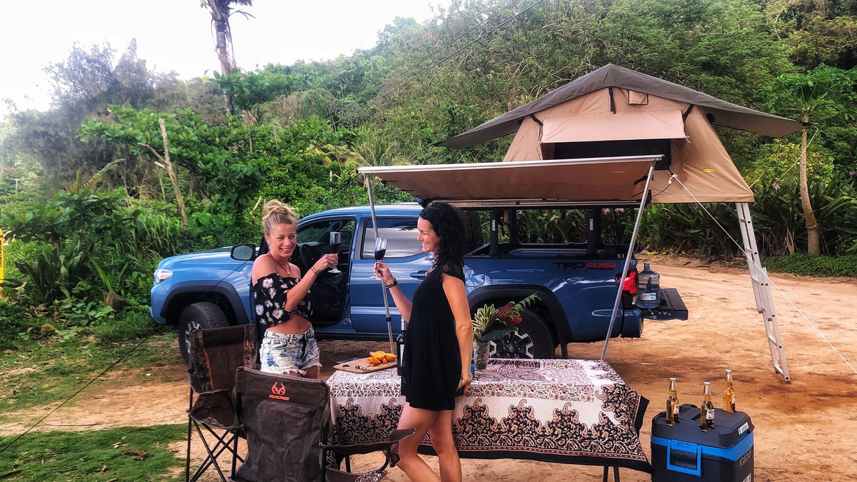 Women toast by a truck with a rooftop tent and awning, offering an outdoor camping trip, similar to an RV rental. — photo 12