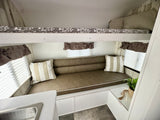 Compact rv rental interior with a cozy lower sofa, upper bunk bed, window blinds, and a small sink area.