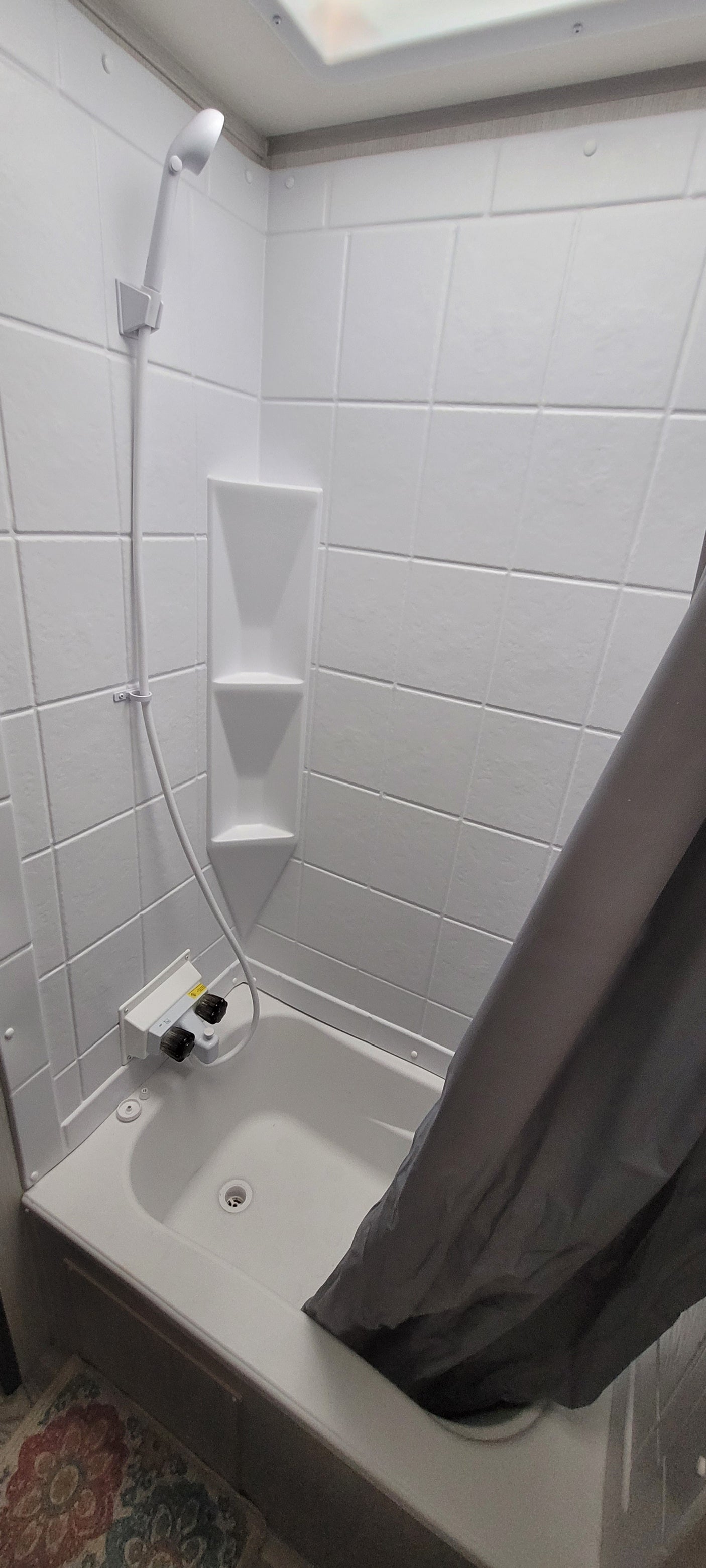 This RV rental offers a clean, compact white shower stall, complete with built-in shelves and a handheld showerhead.