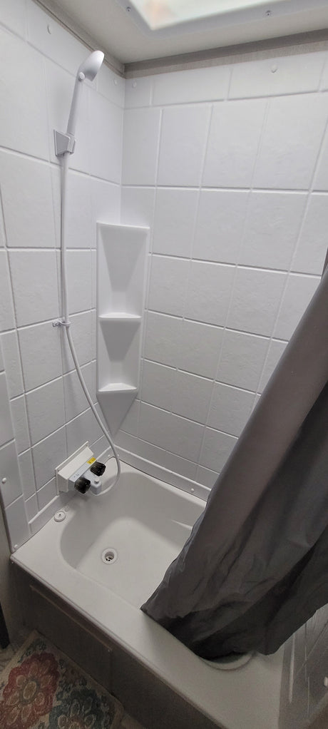 This RV rental offers a clean, compact white shower stall, complete with built-in shelves and a handheld showerhead.