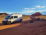 An RV rental van parked in a vibrant desert campsite with striking red rock formations and a picnic area under a clear sky.