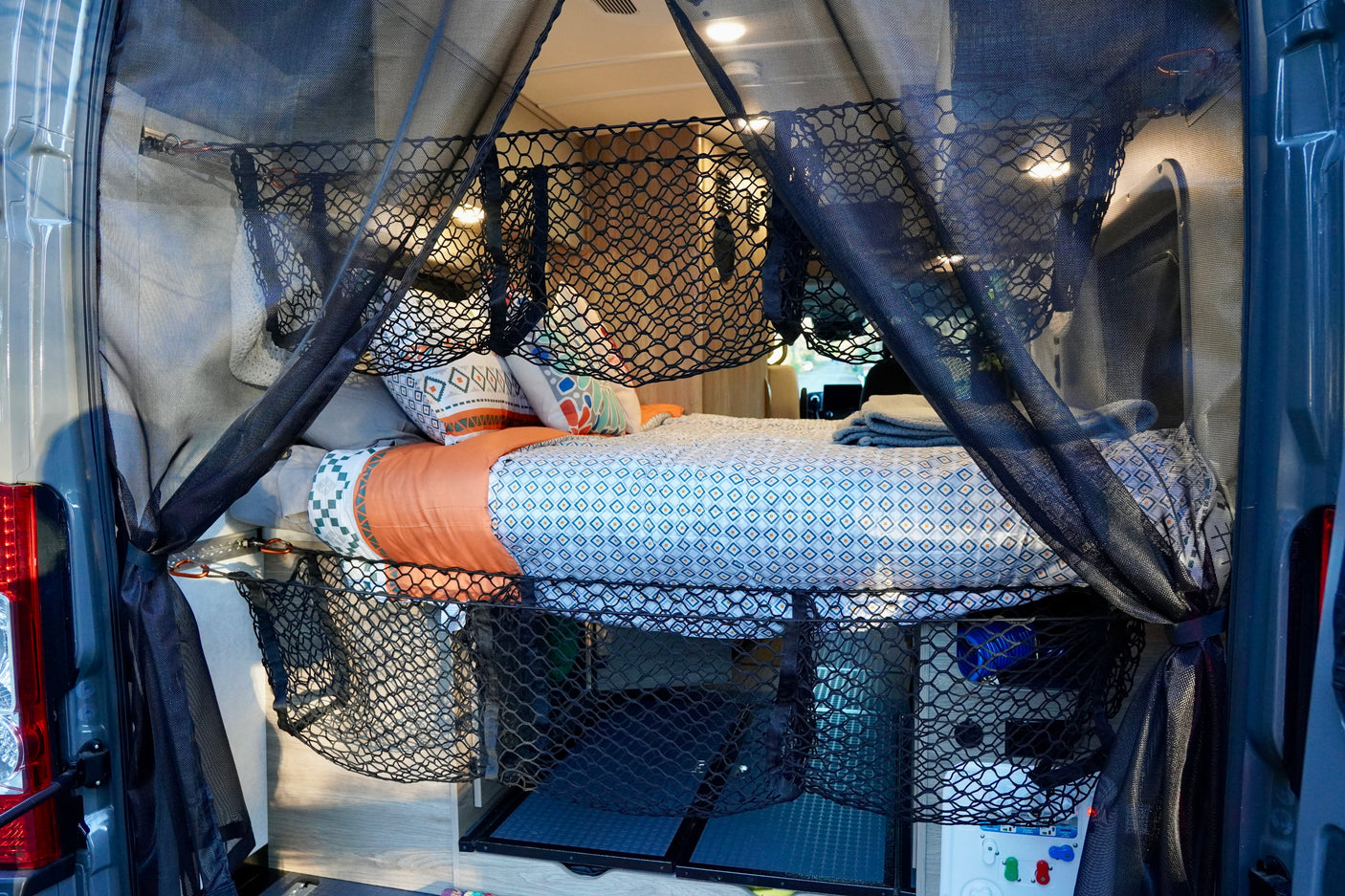 Cozy RV rental bed setup with mosquito net, patterned bedding, & under-bed storage nets. Ideal for van life.