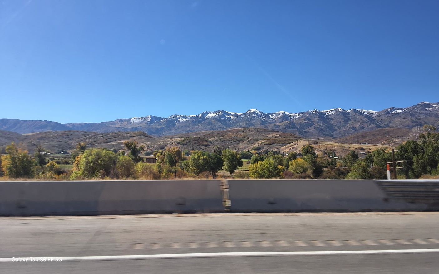 Snow-capped mountains and vibrant autumn trees line a scenic road, ideal for an RV rental adventure under a clear blue sky.
