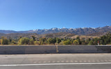 Snow-capped mountains and vibrant autumn trees line a scenic road, ideal for an RV rental adventure under a clear blue sky.