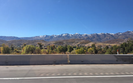 Snow-capped mountains and vibrant autumn trees line a scenic road, ideal for an RV rental adventure under a clear blue sky.