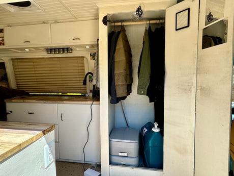 An RV rental's interior: compact kitchenette, wardrobe with hanging clothes, portable toilet, and water jug.