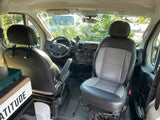 Front cabin of an RV rental van, featuring comfortable driver and passenger seats, dashboard, and a view of the camping setup.