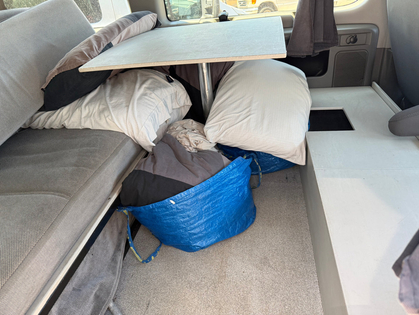 Inside this rv rental, a compact living area features a bed, dining table, and personal belongings stored in blue bags.