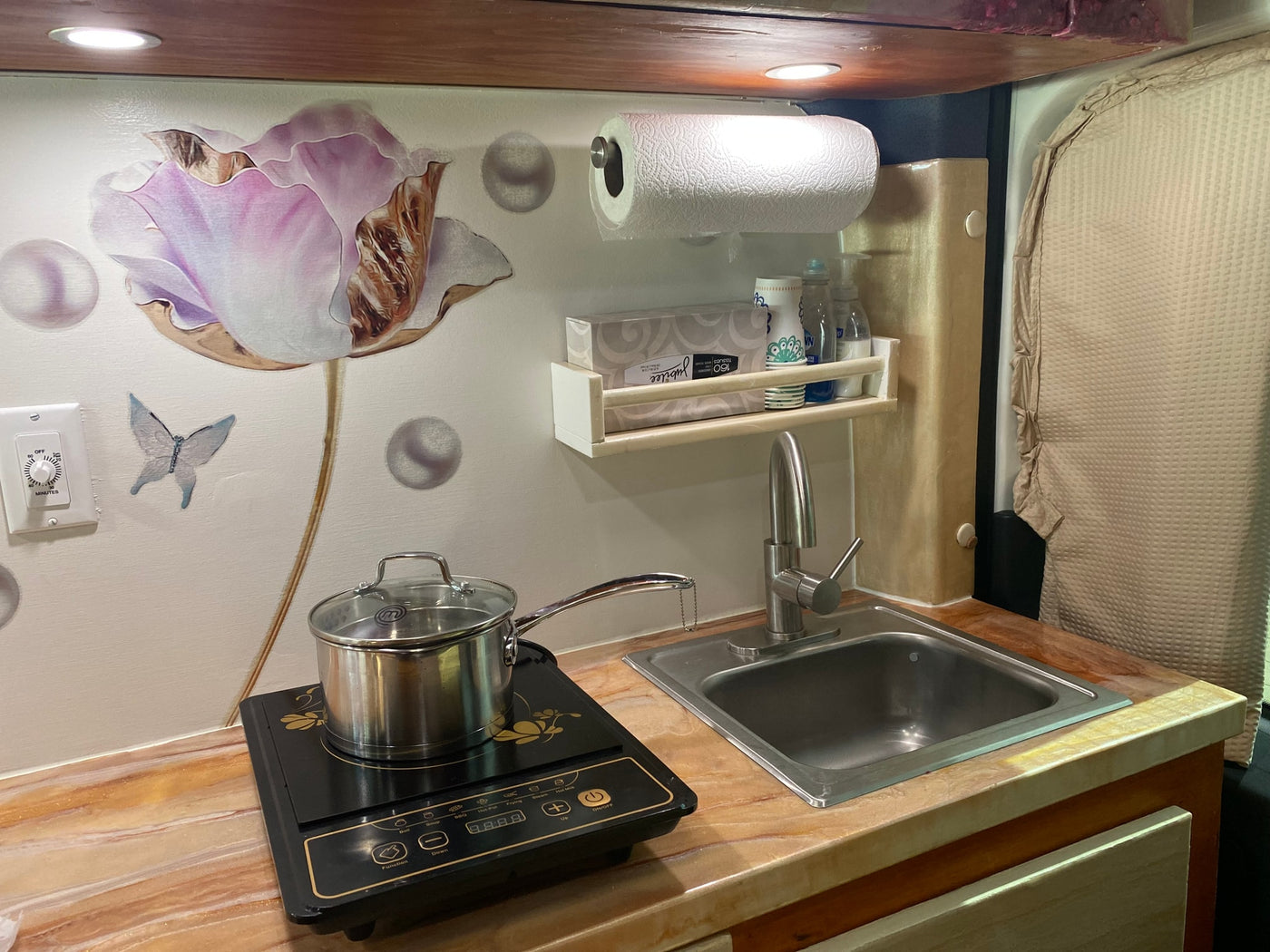 Compact RV rental kitchenette featuring an induction cooktop, sink, and storage shelf, ideal for travel convenience. — photo 8