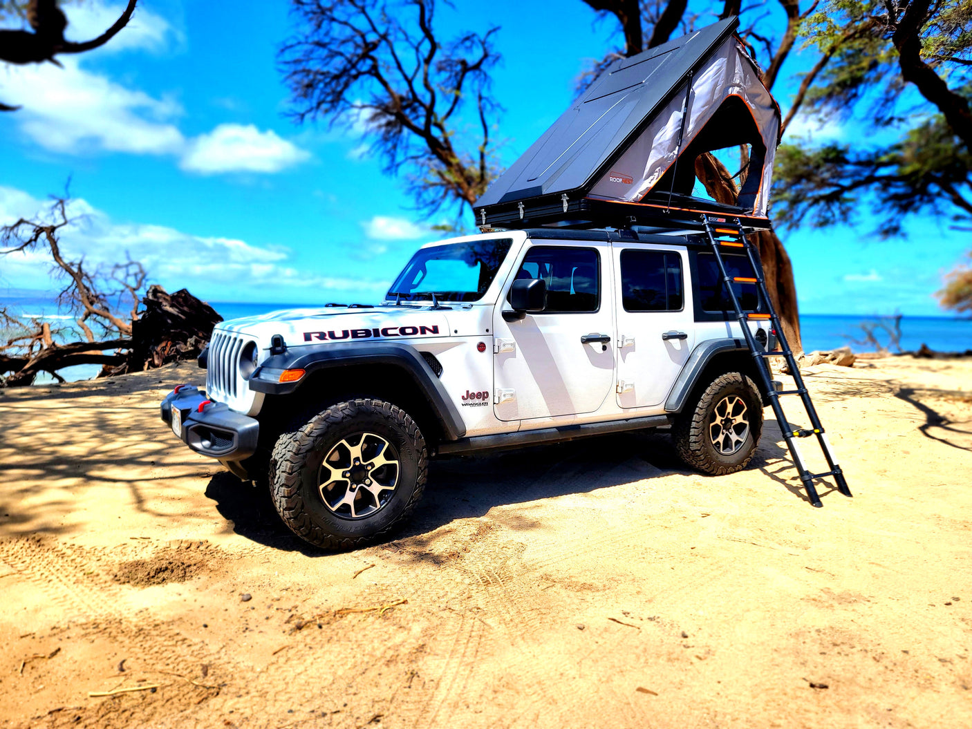 White Jeep Rubicon with Roofnest tent & ladder on sandy beach by the ocean. Your perfect rv rental adventure!