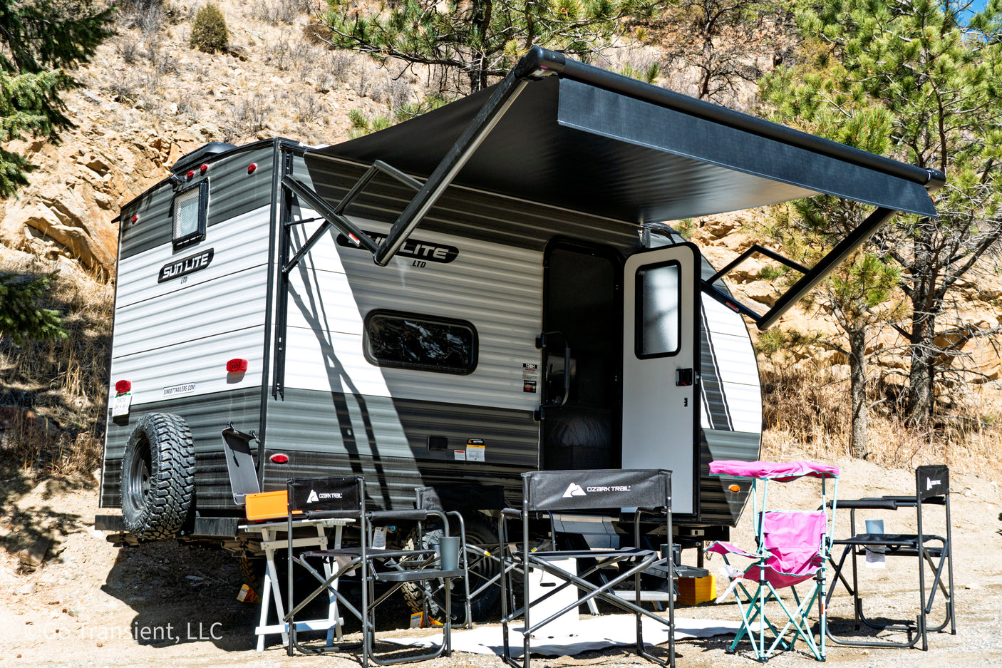 RV rental ready for outdoor camping: A travel trailer with an extended awning, chairs, and tables set up in nature.