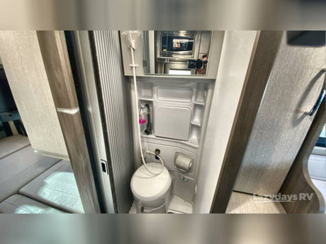 Compact RV rental wet bath with toilet, shower, and mirror. Adjacent sleeping area visible for camper comfort.