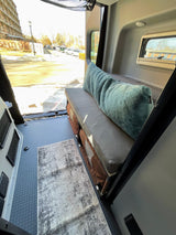 This RV rental features comfortable bench seating with storage below, a floor rug, and an outdoor view.