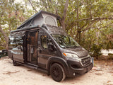 This dark gray pop-top RV rental camper van is parked at a scenic campsite, ready for your outdoor travel adventure.