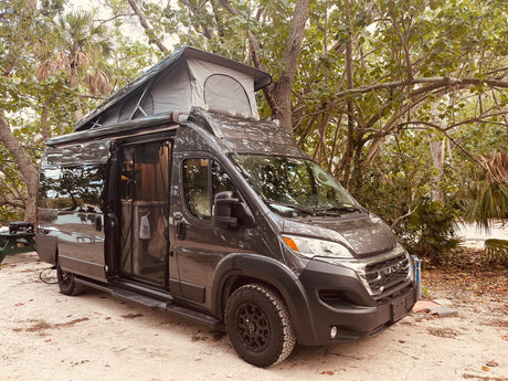 This dark gray pop-top RV rental camper van is parked at a scenic campsite, ready for your outdoor travel adventure.