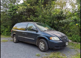 Dark blue minivan on gravel, an alternative to an RV rental. Surrounded by lush greenery, ready for travel.