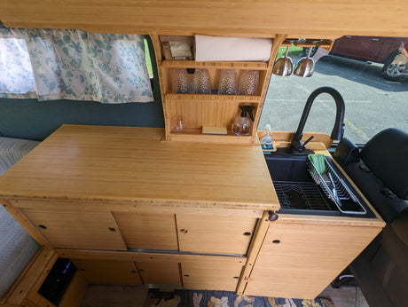 Inside an RV rental: a custom bamboo kitchen with sink, faucet, shelves, and ample storage for a comfortable journey.