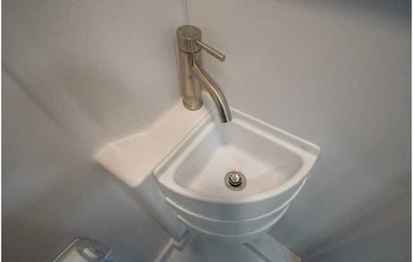 A sleek, space-saving corner sink with a modern faucet, perfect for an RV rental's compact bathroom.