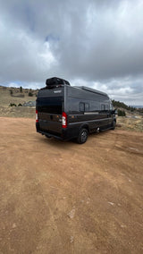 Dark grey camper van (Winnebago Solis) parked on a dirt road under cloudy skies. Perfect for an RV rental adventure.