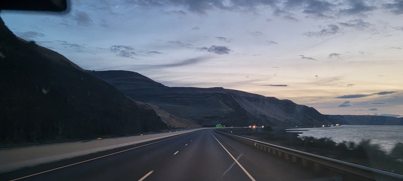 A scenic highway at dusk, winding past dark mountains and a shimmering lake. Ideal for an RV rental adventure.