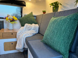 This inviting rv rental interior features a grey sofa with green pillows, a soft blanket, and fresh flowers on a side table.