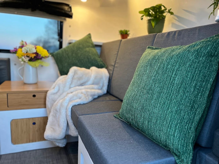  with its cozy seating and scenic window views.|Cozy campervan RV rental setup: two champagne flutes & a plant on a table