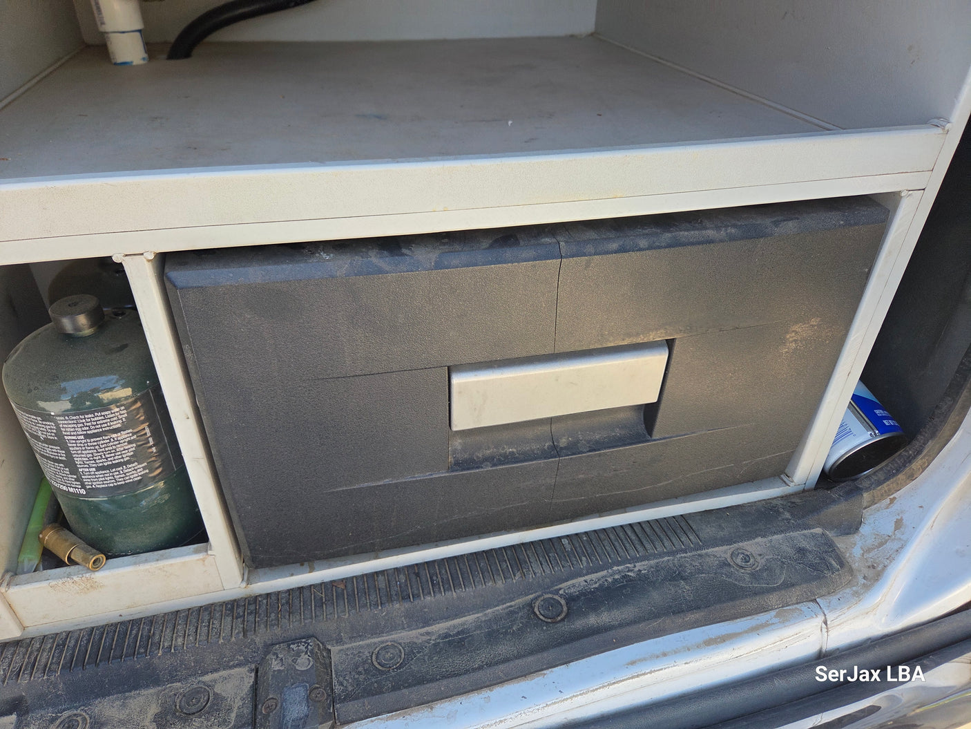 RV rental: A portable fridge, a green propane tank, and other supplies are neatly stored in a van's custom interior.