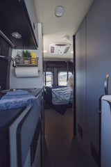 This RV rental interior showcases a compact kitchen area on the left and a cozy bedroom with rear window views, ideal for mobile living.
