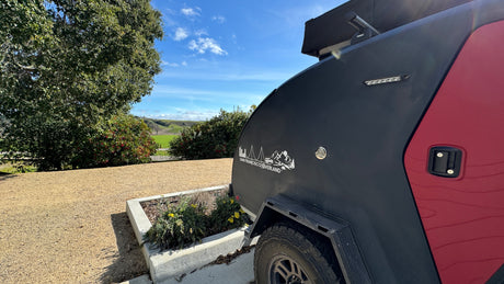 San Francisco Overland teardrop trailer RV rental parked with a scenic view of green hills & blue sky. Ideal for adventure.