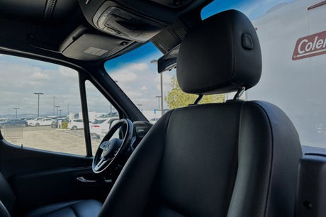 Mercedes-Benz RV rental interior: black seats, steering wheel, dashboard. Outside view of lot. Adventure awaits.