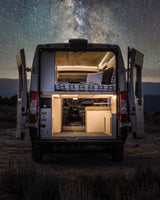 Experience adventure with an RV rental! This camper van, with its lit interior and bed, is parked under a stunning starry night sky.