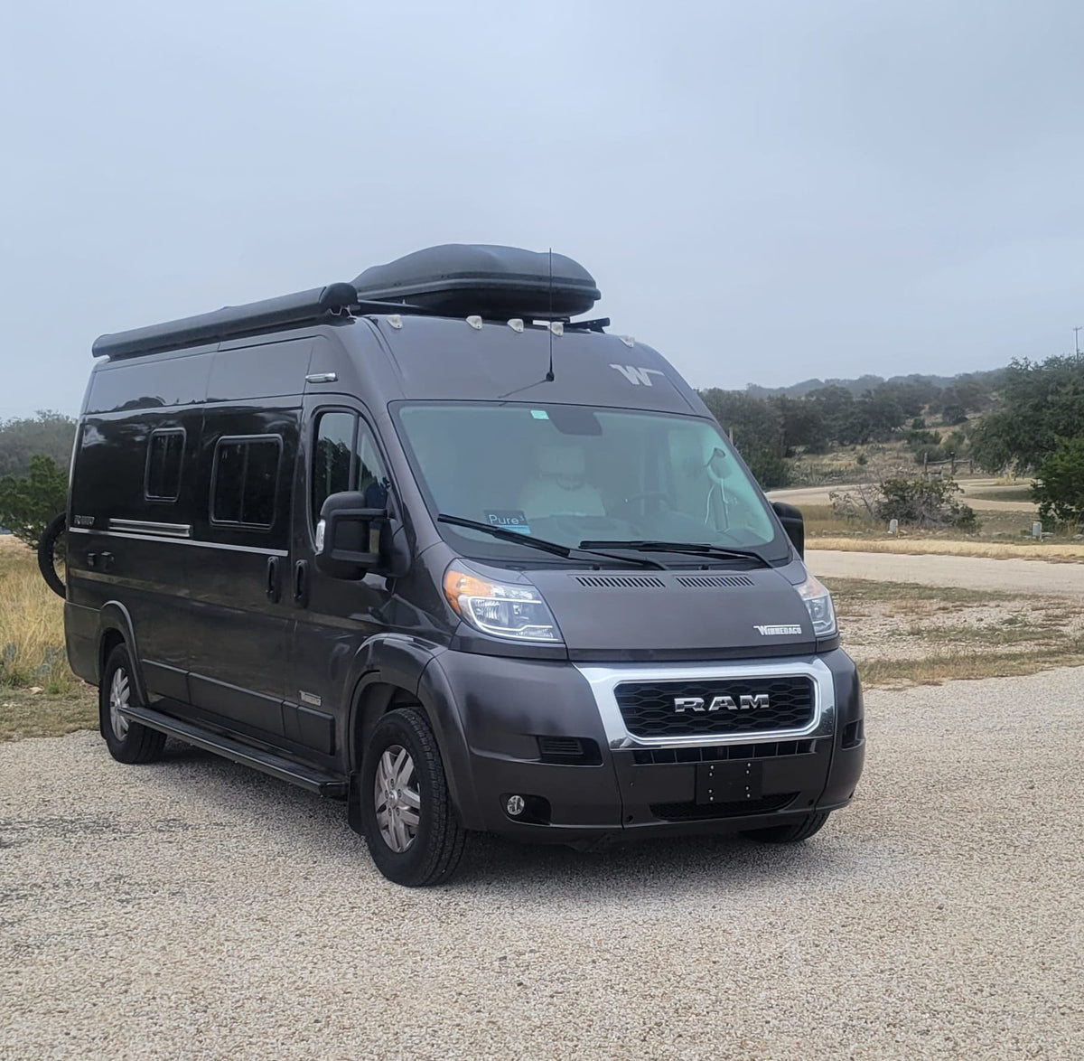 Dark grey Winnebago Ram ProMaster camper van RV rental on gravel. Ready for camping and travel adventures.|Inside a cozy rv rental