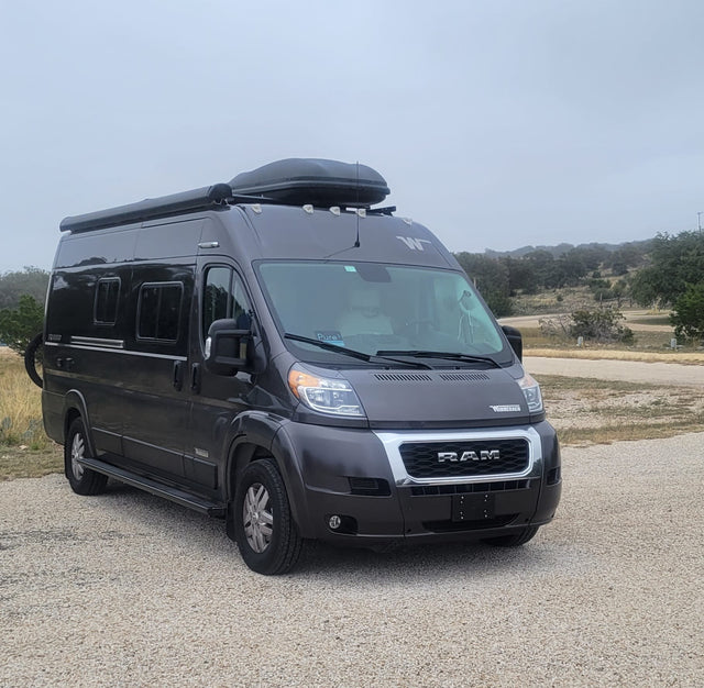 Dark grey Winnebago Ram ProMaster camper van RV rental on gravel. Ready for camping and travel adventures.