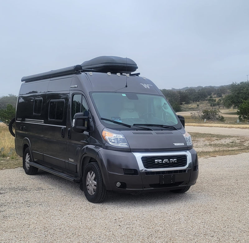 Dark grey Winnebago Ram ProMaster camper van RV rental on gravel. Ready for camping and travel adventures.|Inside a cozy rv rental — photo 1