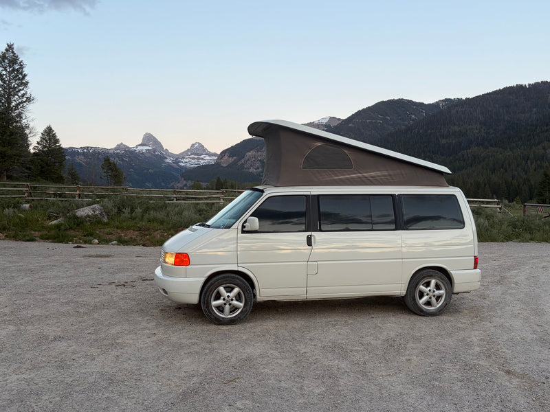 White VW pop-top camper van RV rental on gravel, with snowy mountains & pines in the distance. — photo 10
