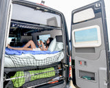 Enjoy an RV rental! A woman relaxes reading in a spacious camper van with open rear doors, revealing cozy bed & storage.