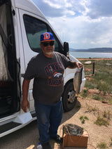 Man with his fishing catch next to an RV rental, by a lake under cloudy skies.