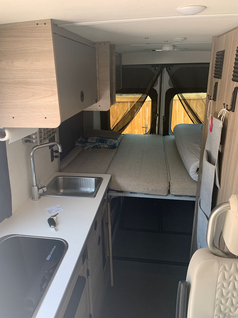 parked in a sunny forest.|Inside an RV rental: a compact camper van interior featuring a bed — photo 1