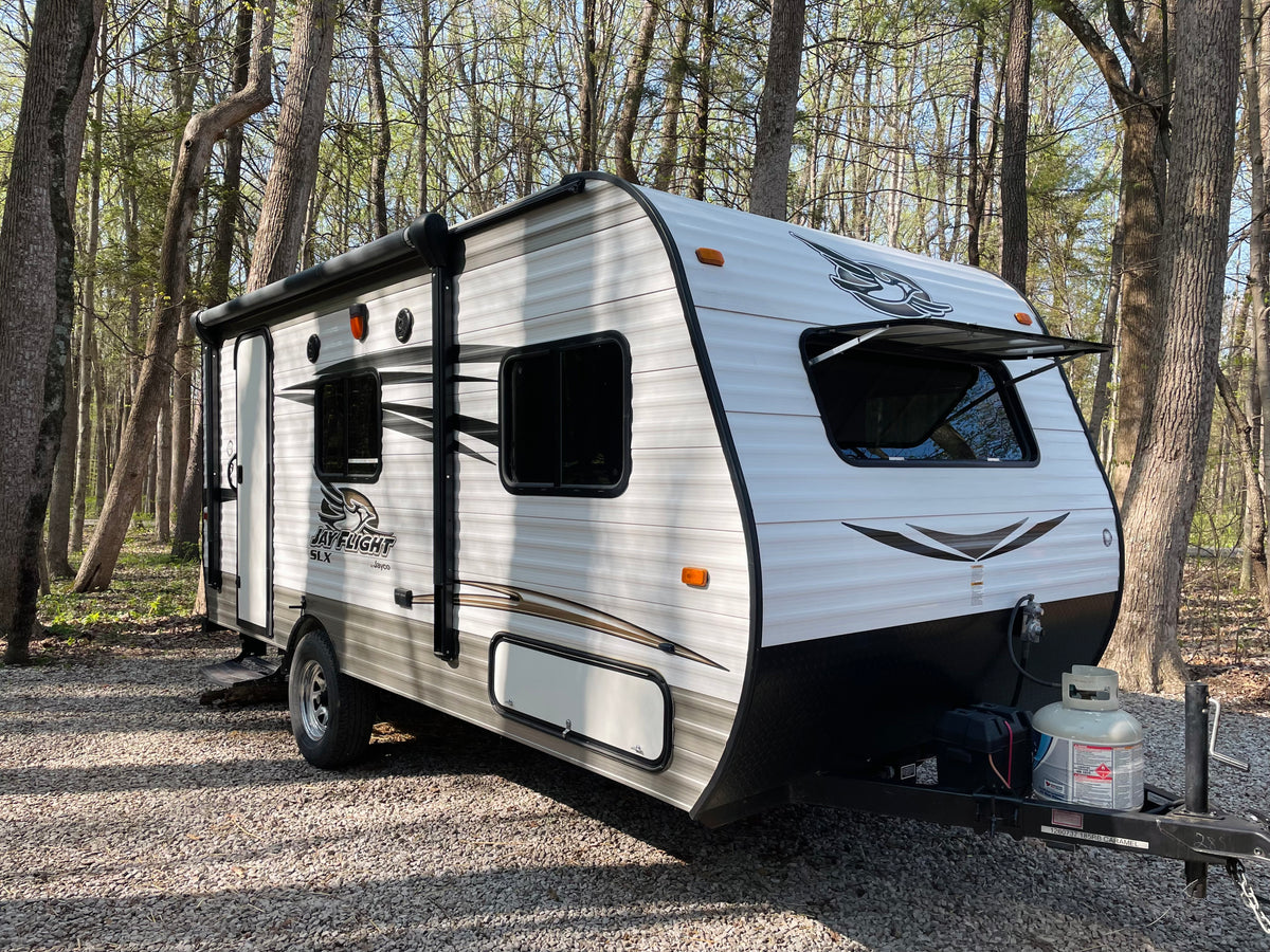 White Jay Flight SLX travel trailer at a wooded campsite, ready for your next RV rental adventure.