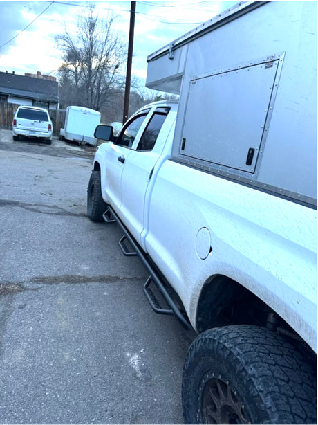 Dirty white pickup truck featuring a custom, rugged camper body with off-road tires. Ideal for adventurous RV rental trips.