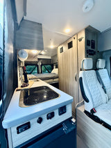 Spacious RV rental interior with a functional kitchen, comfortable bed, and quilted swivel seats. Ready for your road trip!