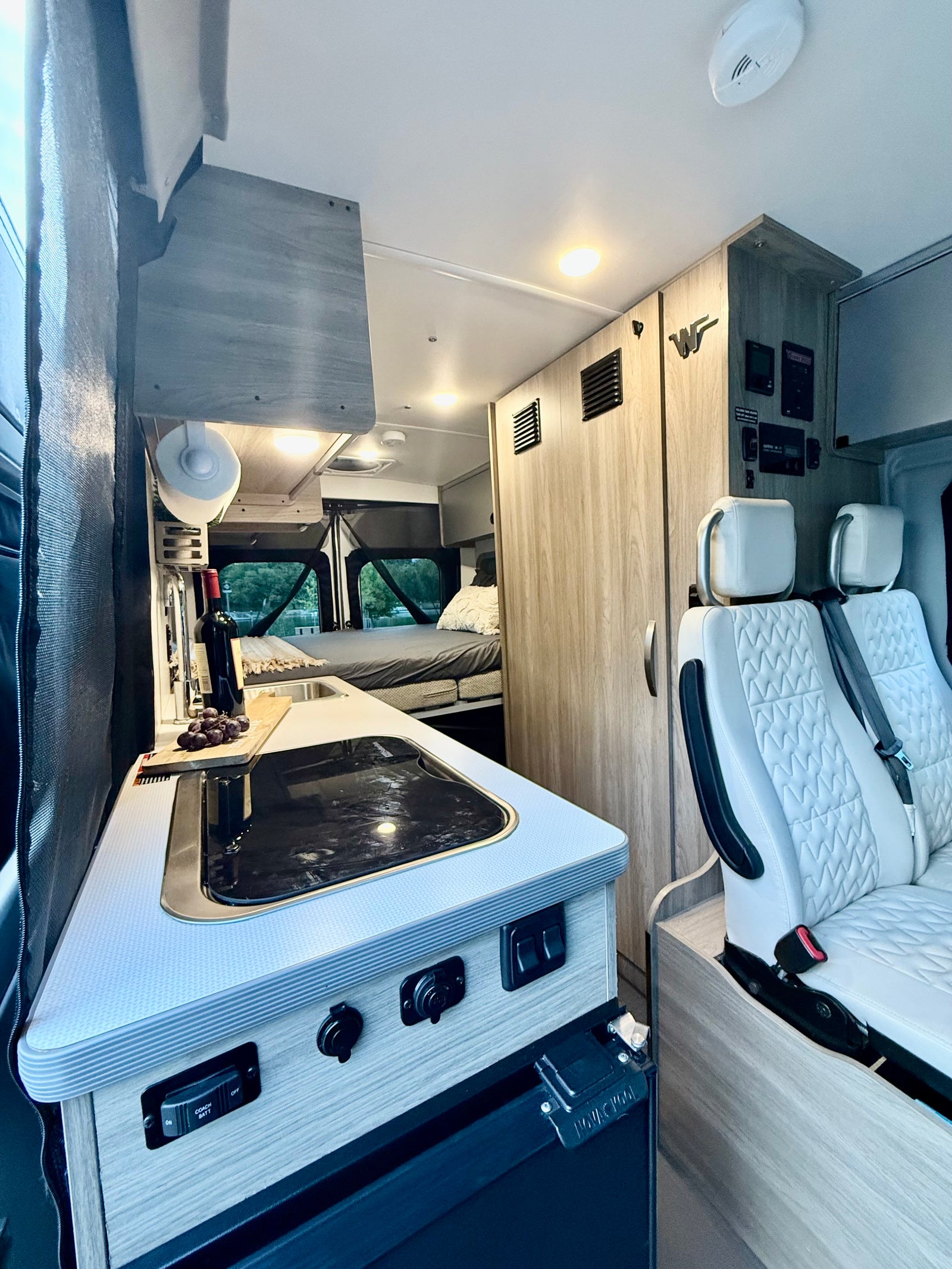 Spacious RV rental interior with a functional kitchen, comfortable bed, and quilted swivel seats. Ready for your road trip!