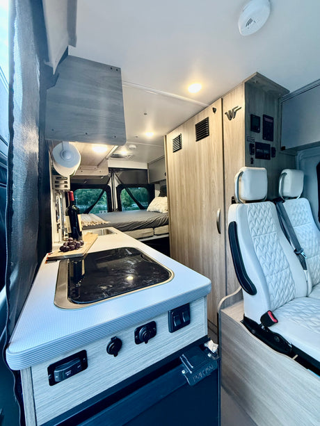 Spacious RV rental interior with a functional kitchen, comfortable bed, and quilted swivel seats. Ready for your road trip!