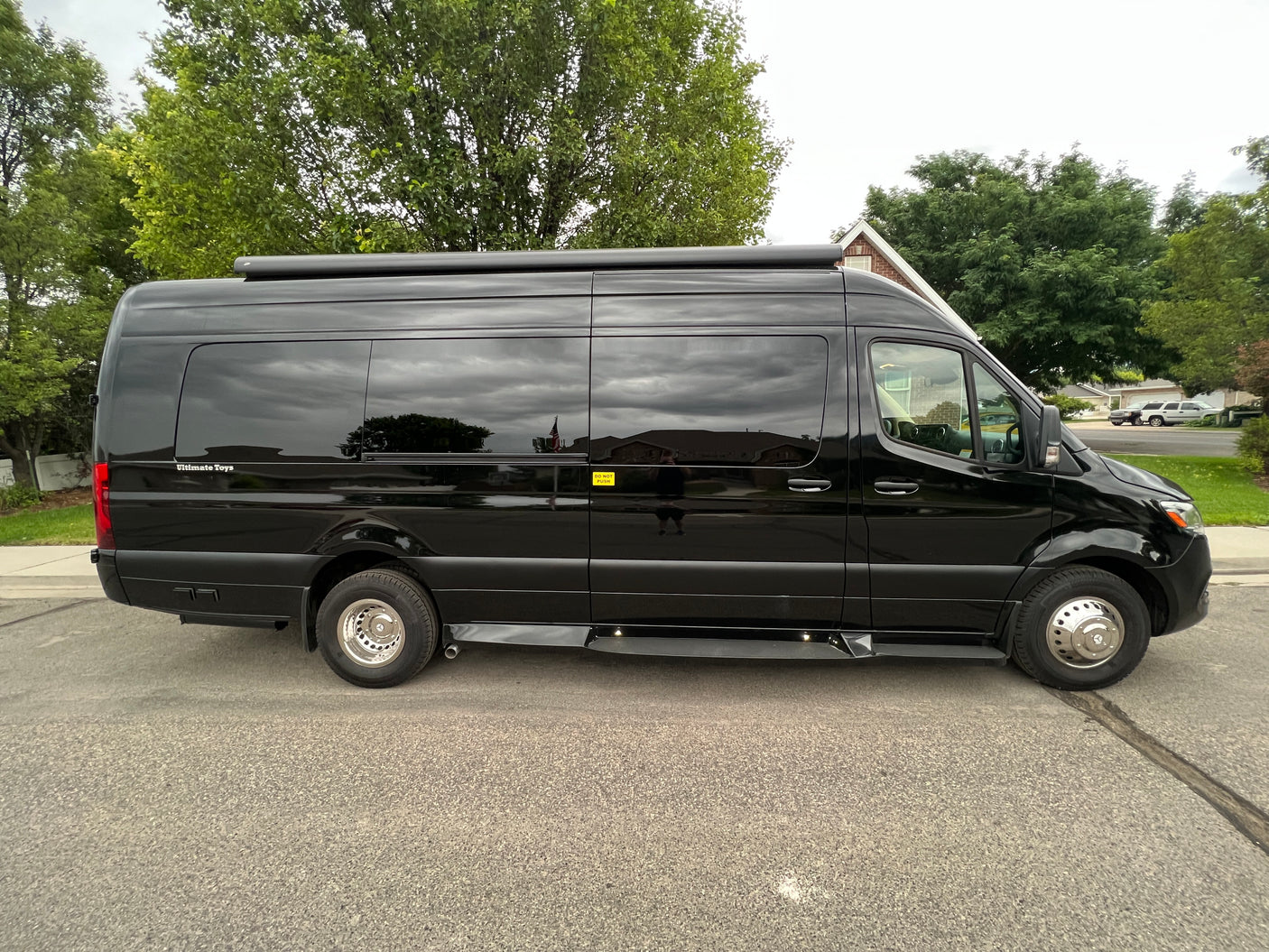 A sleek black Mercedes-Benz Sprinter van, ideal for an RV rental, is shown with tinted windows and a roof awning.