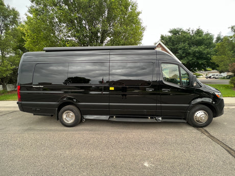 A sleek black Mercedes-Benz Sprinter van, ideal for an RV rental, is shown with tinted windows and a roof awning.