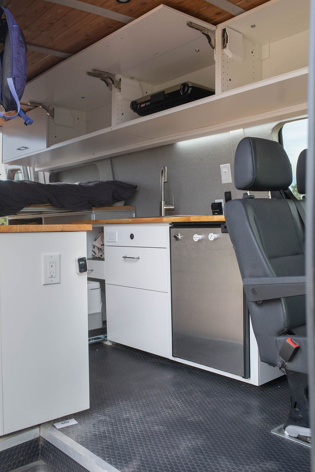 Compact rv rental interior with kitchen, bed, overhead storage, and fridge. Ideal for mobile living.