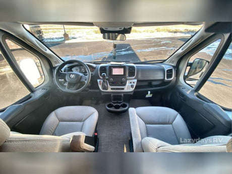 Spacious front cab interior of an RV rental, featuring the steering wheel, dashboard, and light-colored seats.