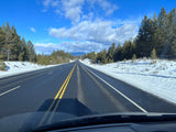Open highway framed by snowy pine trees under a clear blue sky, perfect for your next rv rental road trip.