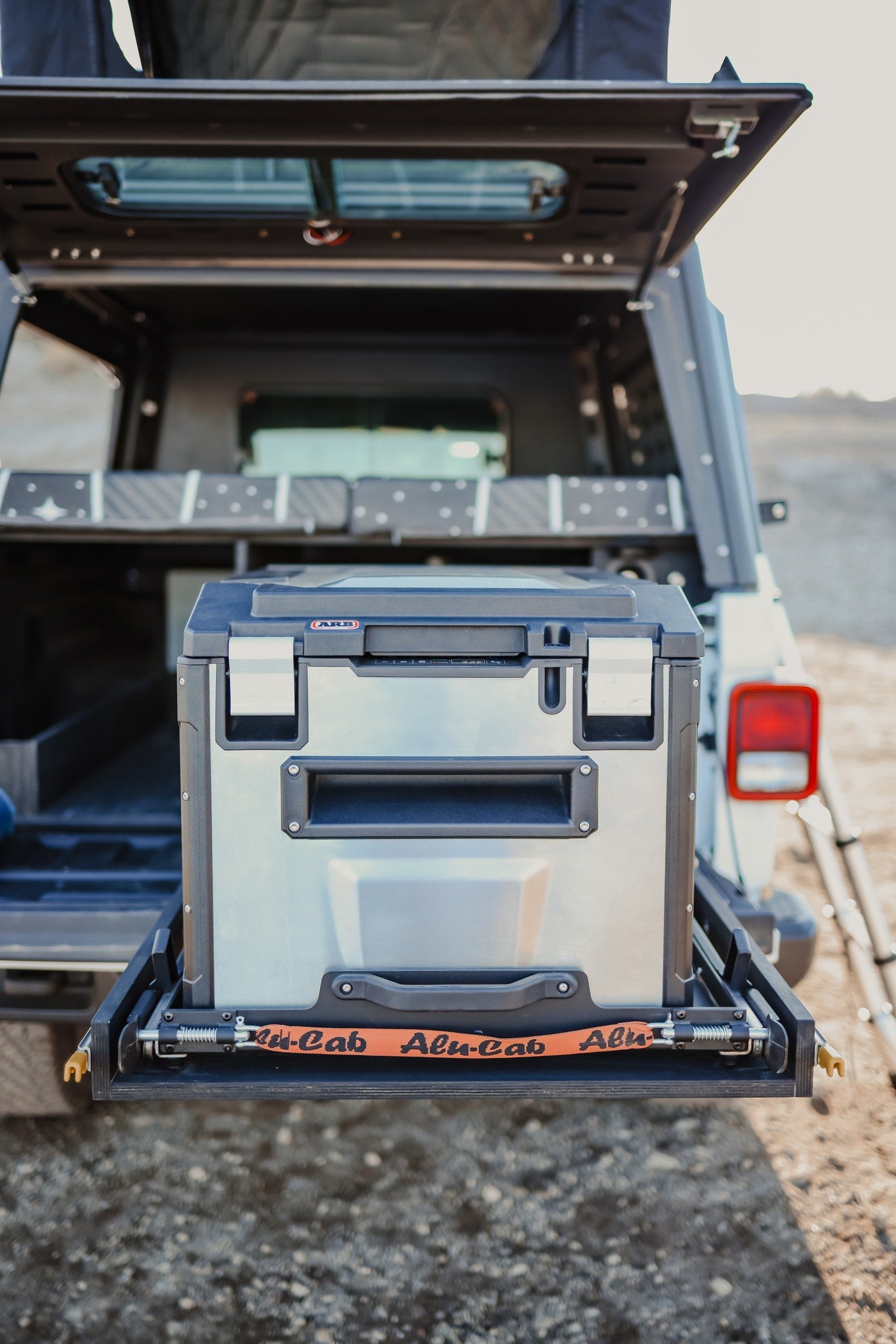Adventure RV rental setup: ARB fridge on a pull-out slide, secured with an Alu-Cab strap in an open vehicle rear. — photo 16