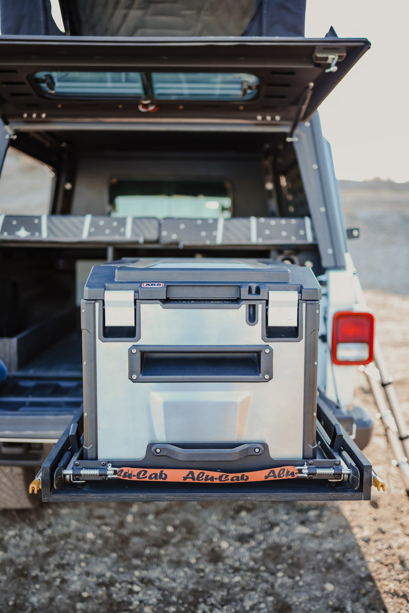 Adventure RV rental setup: ARB fridge on a pull-out slide, secured with an Alu-Cab strap in an open vehicle rear. — photo 16